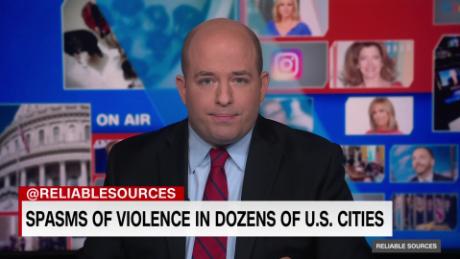 A bald man in the center of a CNN broadcast with stock images projected on a greenscreen behind him. A chyron reads "@RELIABLESOURCES: SPASMS OF VIOLENCE IN DOZENS OF U.S. CITIES"